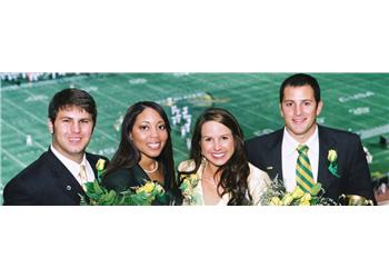 four smiling graduates in regalia on a field