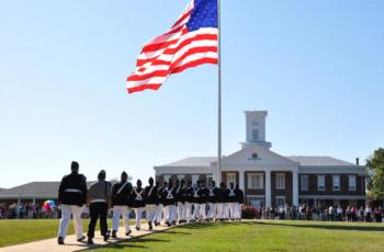 marching band in uniform in front of building with american flag