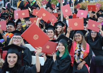 graduates in caps and gowns holding red diploma covers celebrating