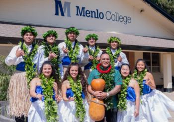 Menlo College students posing in front of campus sign during luau celebration.