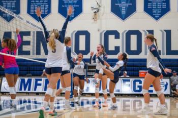 The Menlo College volleyball team celebrating with excitement on the court. 
