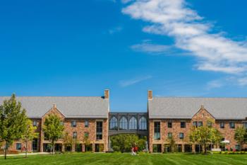 Two brick buildings with an arched glass walkway under a blue sky.