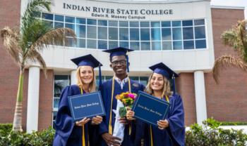 graduates in caps and gowns smiling with diplomas in front of indian river state college