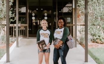two students smiling in front of a building