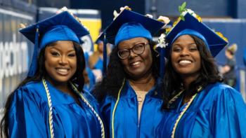 three graduates in blue caps and gowns smiling at the camera