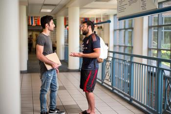 two male students conversing in a corridor