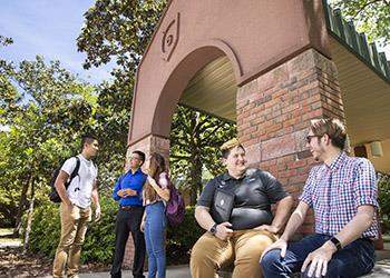 students socializing by a campus entrance arch