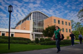 students walking by a modern campus building with trees