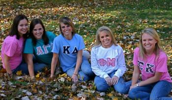 group of women sitting on autumn leaves wearing sorority shirts