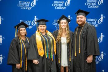 graduates in caps and gowns pose in front of illinois central college backdrop