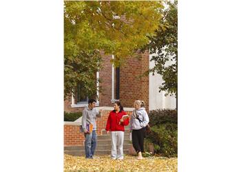 three people talking beside a brick campus building
