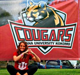 person making heart sign in front of 'cougars iu kokomo' banner