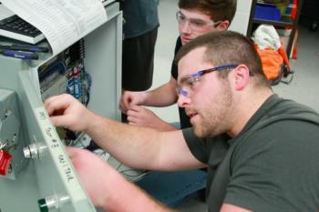 students working on an electrical panel wearing safety glasses