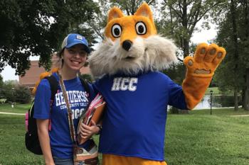 student and mascot wearing blue 'hcc' shirts outside on campus