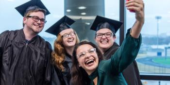 graduates in caps and gowns smiling for a selfie indoors