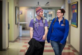 two students walking in a college hallway with backpacks