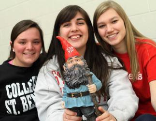 three students holding a mascot gnome in college apparel