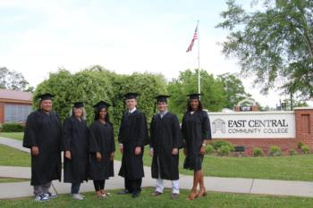 graduates in caps and gowns near east central community college sign