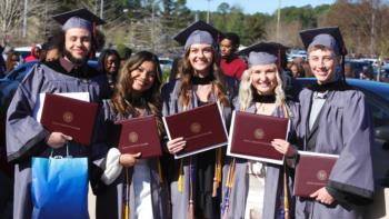 smiling graduates in caps and gowns holding diplomas at hinds community college