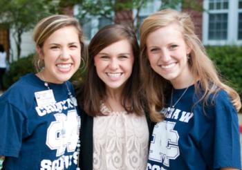 three smiling people wearing university t-shirts