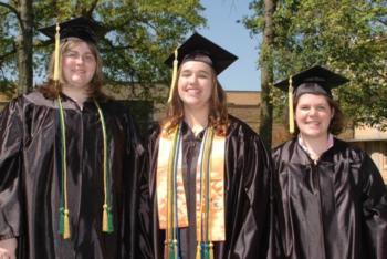 three graduates smiling in cap and gown outdoors