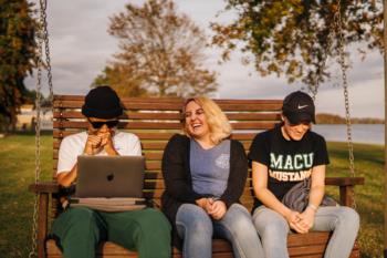 three students laughing on a swing bench
