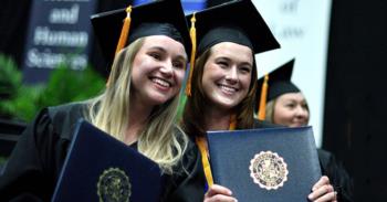 graduates smiling in caps and gowns holding diplomas