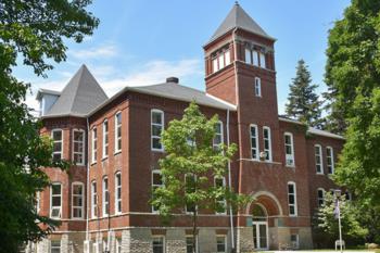 historic brick building with a tall tower and lush greenery