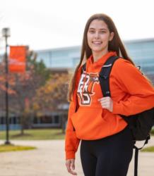 student in orange hoodie with backpack on campus