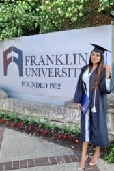 graduate in gown holding diploma near franklin university sign