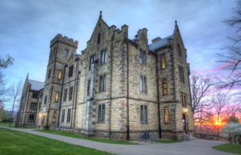 stone building with lit windows at sunset on a college campus
