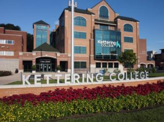 brick building with 'kettering college' sign and flowerbed in front