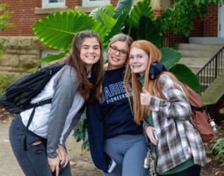 three students smiling on campus with backpacks