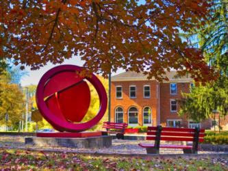 red sculpture and benches beneath autumn trees on campus