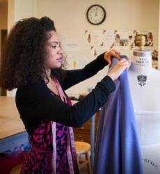 student draping fabric on a mannequin with a tape measure around her neck
