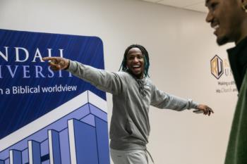 student joyfully gesturing in front of randall university banner