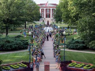 students line a pathway with an american flag and building in background