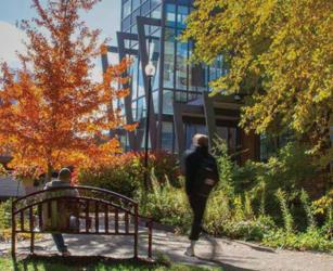 campus building with autumn trees and a park bench
