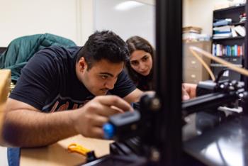Two people focus intently on a project or device they are adjusting or setting up.