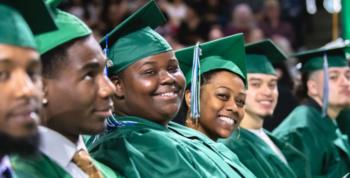 students in green caps and gowns smiling at a graduation ceremony