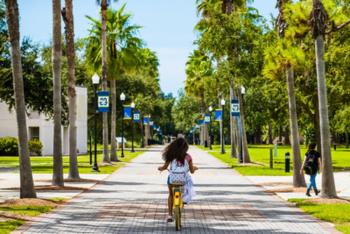 student biking along a tree-lined campus pathway