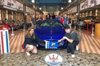 group posing with a blue car in a museum