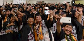 graduates wearing caps and gowns take selfies in a crowded hall