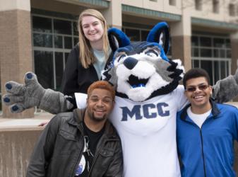 students posing with mascot wearing 'mcc' shirt outside building