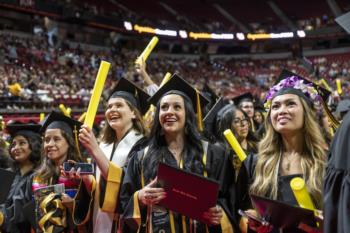 graduates in caps and gowns holding diplomas and cheering