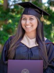 graduate in cap and gown holding diploma with outdoor backdrop
