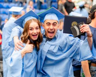 two graduates in blue gowns celebrating